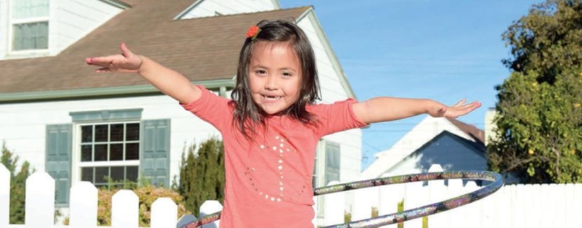 Smiling child hula hooping in front of a house